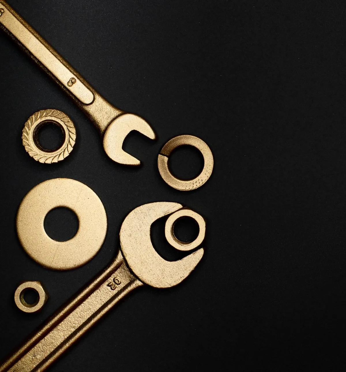 Brass wrenches, washers and nuts laid out on a dark surface.